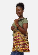 A person holding a tote bag with an African print and faux leather straps.