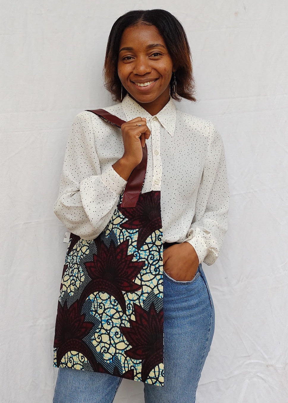A person holding a tote bag with an African print and faux leather straps.